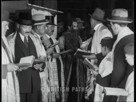 British Pathé frame: men and boys in talleisim and hats; one holds a Torah scroll with a Magen David on the mantle