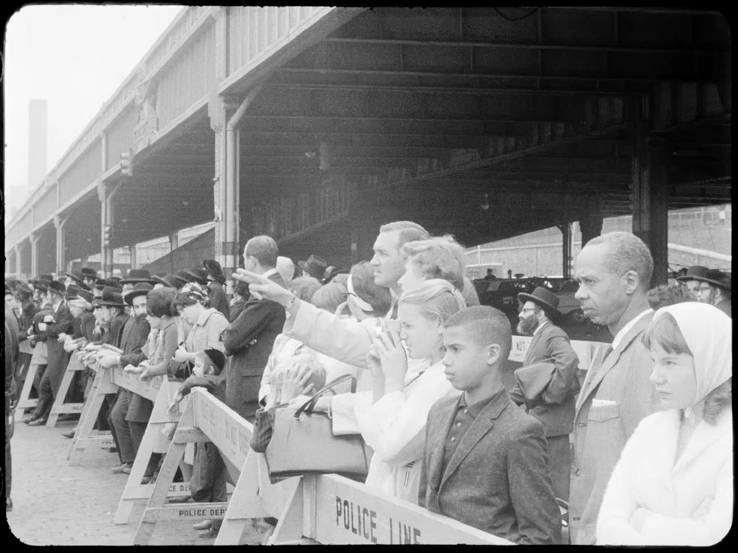People wait along the pier shed behind a police line, with chassidim farther down the line